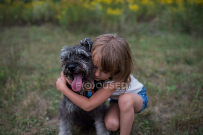 Маленькая девочка обнимает собаку на травяном поле — стоковое фото