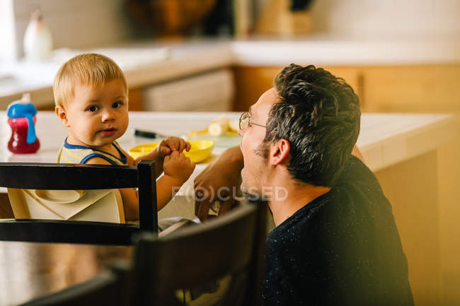 Padre ayudando a su hijo pequeño a la hora de comer - foto de stock