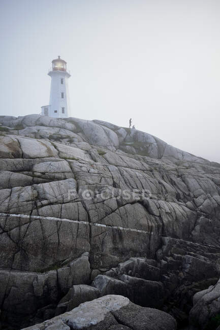 Pareja en las rocas por el faro, Peggy 's Cove, Nueva Escocia, Canadá - foto de stock