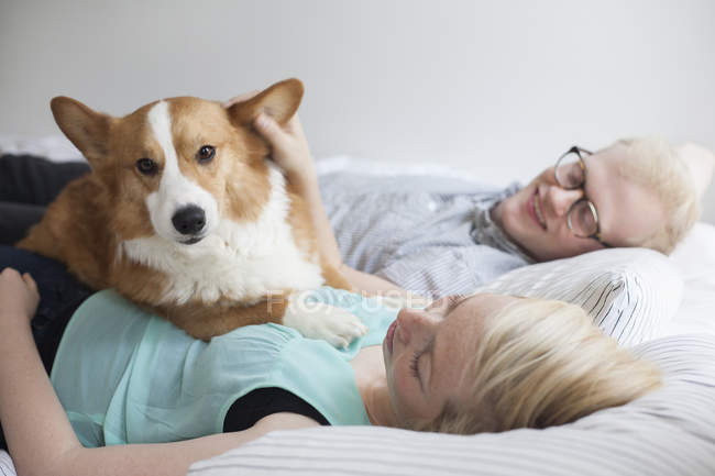Cute corgi dog lying on bed with young couple — Stock Photo