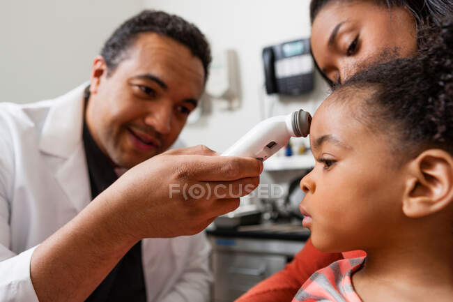 Mid adult doctor using medical equipment on young patient — Stock Photo