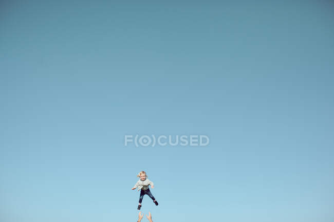Weite Sicht auf weibliches Kleinkind, das mitten in der Luft gegen weiten blauen Himmel geschleudert wird — Stockfoto