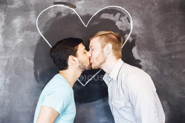 Couple masculin baisers devant tableau noir avec coeur de craie — Photo de stock