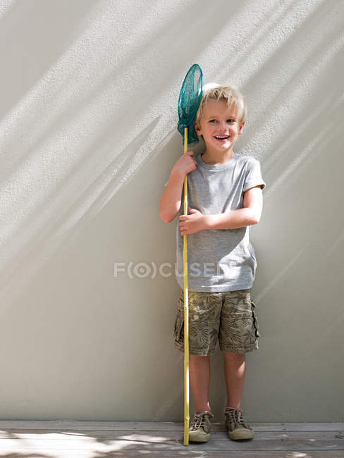 Niño de pie junto a la pared con red de pesca, retrato - foto de stock