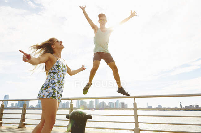 Молодой человек прыгает в воздухе на солнечной набережной, Нью-Йорк, США — стоковое фото