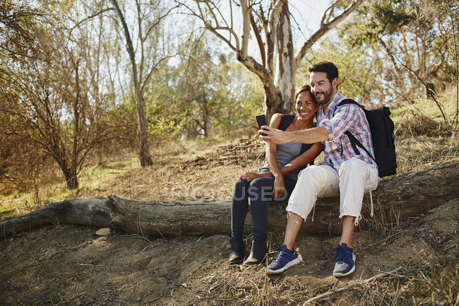 Paar wandert, sitzt auf Baumstamm und macht Smartphone-Selfie — Stockfoto