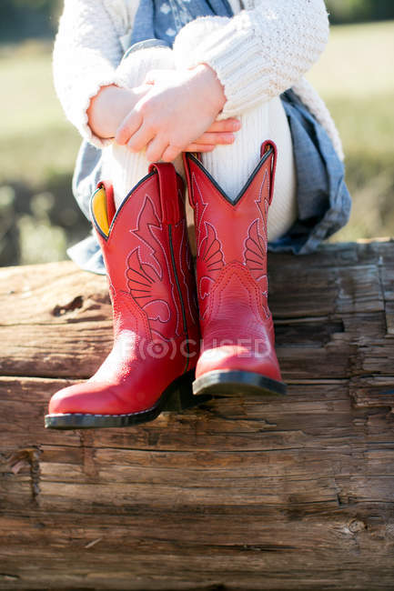 Neck down view of girl sitting on log wearing red cowboy boots — Stock Photo