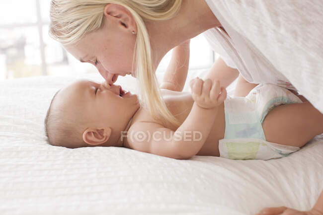 Mujer adulta media nariz a nariz con hijo bebé acostado en la cama - foto de stock