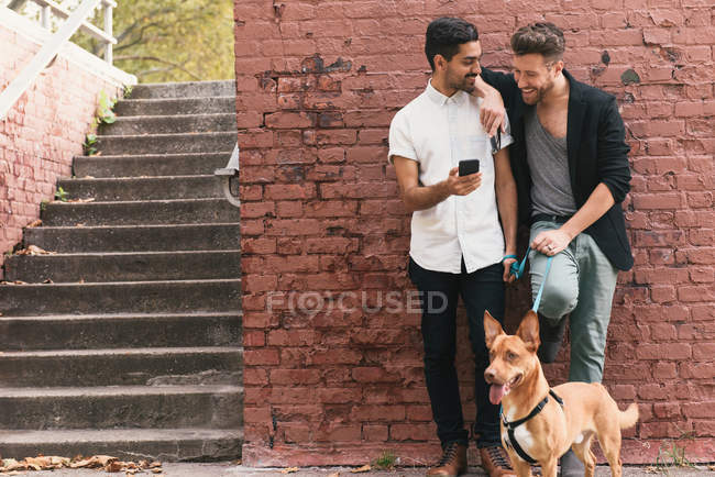 Young male couple leaning against wall and reading smartphone — Stock Photo