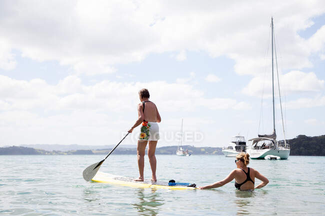Figlia spingendo le madri anziane paddleboard in mare — Foto stock