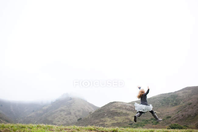 Landscape view of girl in tutu jumping mid air — Stock Photo
