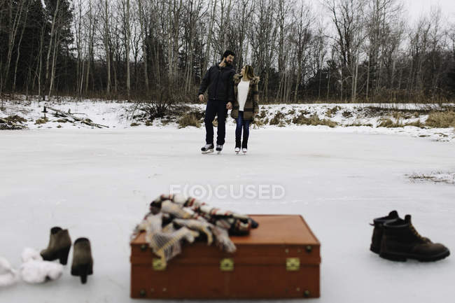 Maleta roja, botas, chal, patinaje de pareja en el fondo, Whitby, Ontario, Canadá - foto de stock