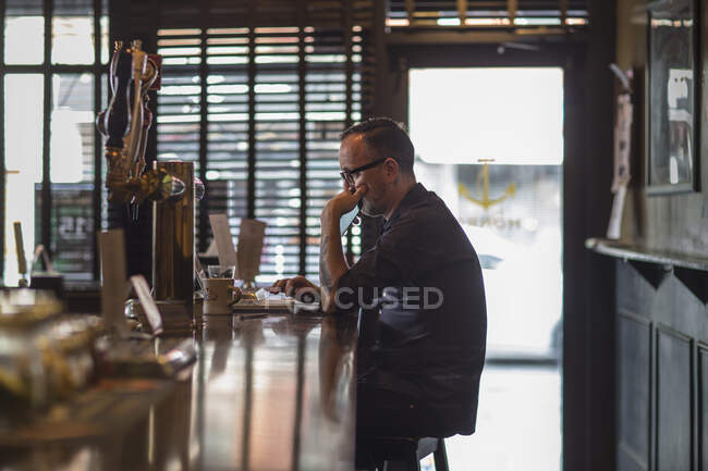 Barman typing on laptop at public house counter — Stock Photo