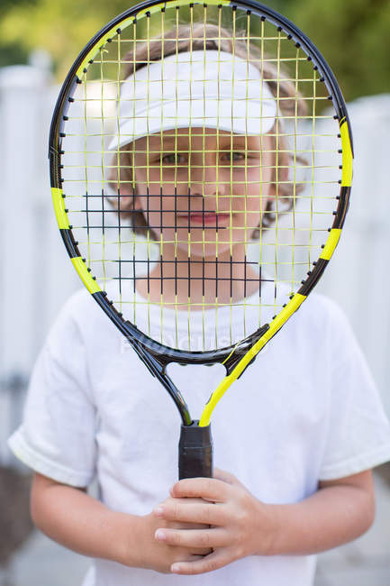 Portrait of boy holding tennis racket in front of face — Stock Photo
