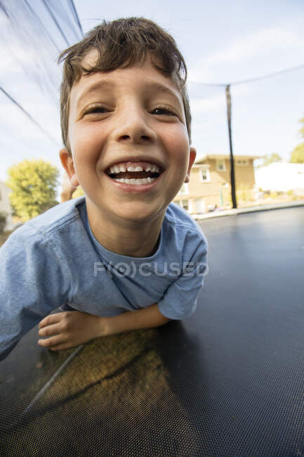 Portrait of young boy leaning on large trampoline, laughing — Stock Photo