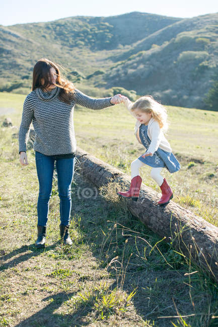 Mitte erwachsene Frau hält Tochter die Hand, während sie vom Baumstamm springt — Stockfoto