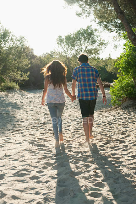 Jeune couple marchant à travers le sable, vue arrière — Photo de stock