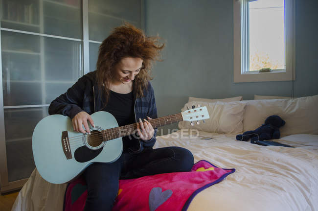 Adolescente tocando la guitarra en el dormitorio - foto de stock