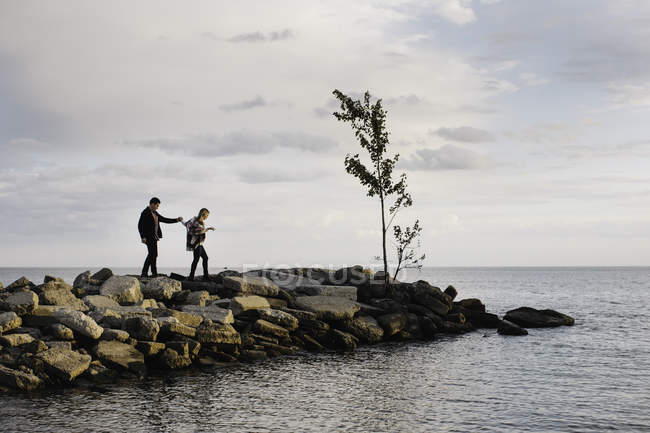 Giovane coppia che cammina sulle rocce accanto al mare — Foto stock