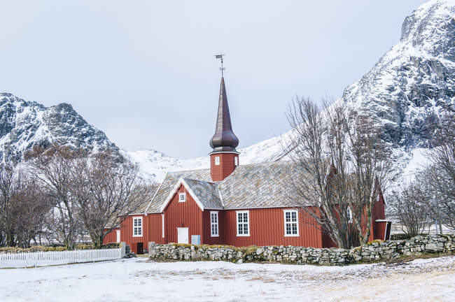 Iglesia tradicional de madera contra rocas cubiertas de nieve, Reine, Lofoten, Noruega - foto de stock