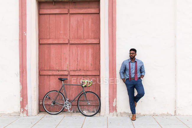 Молодой бизнесмен-велосипедист, прислонившись к стене, ждет — стоковое фото