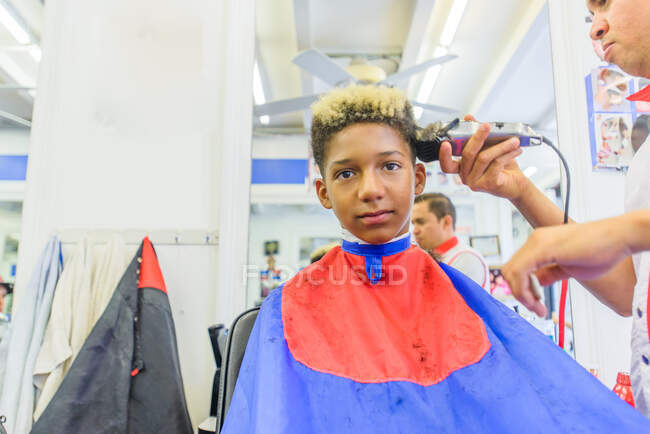 Hairdresser cutting teenage boy's hair in barbershop — Stock Photo