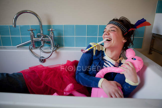 Young woman in bath, wearing costume and blowing party blower — Stock Photo