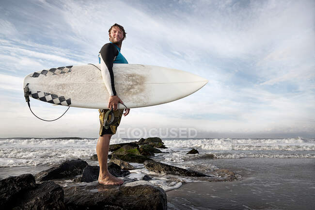 Серфер стоїть на скелях на пляжі — стокове фото