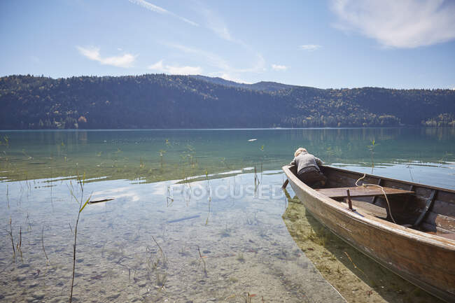 Garçon se penchant vers l'avant du bateau à rames et regardant dans le lac, Kochel, Bavière, Allemagne — Photo de stock