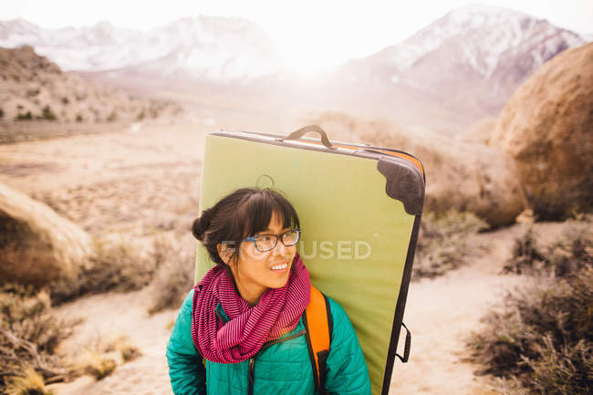 Woman carrying bouldering mat, looking away and smiling, Buttermilk Boulders, Bishop, California, USA — Stock Photo