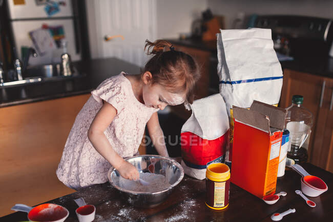 Menina bagunçada na cozinha mexendo tigela de farinha — Fotografia de Stock