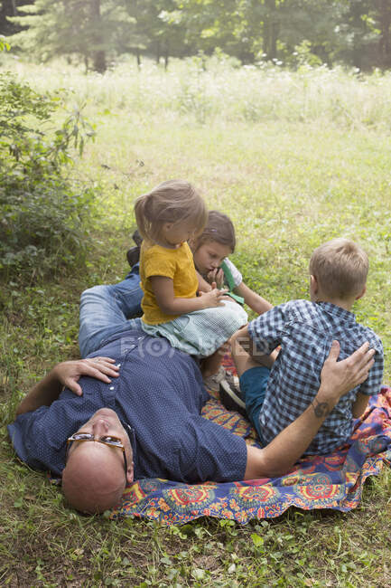 Отец и дети отдыхают на одеяле на траве — стоковое фото