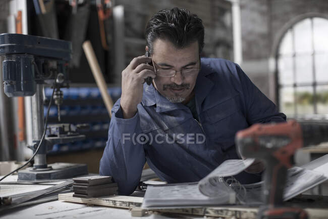 Cape Town, South Africa, machinist on a call while browsing through book in workshop — Stock Photo
