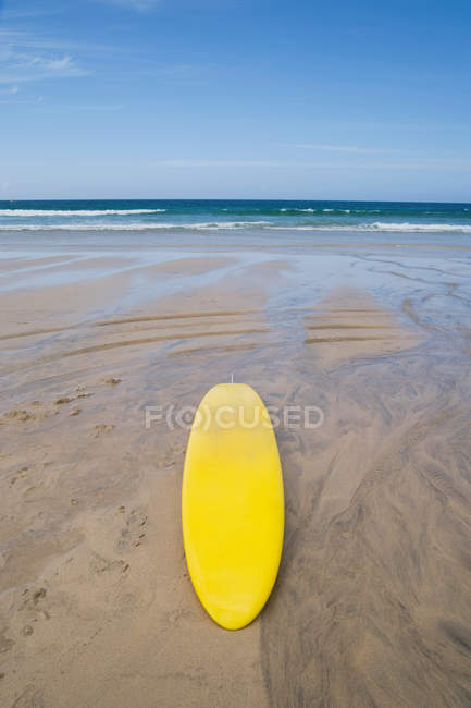 Prancha de surf amarelo na praia de areia à luz do sol — Fotografia de Stock
