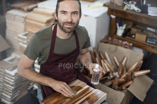 Retrato del hombre aplicando una mancha de madera a la tabla de cortar en fábrica - foto de stock