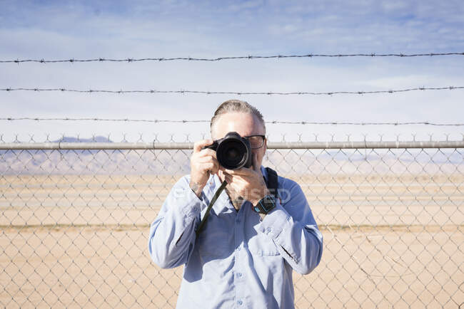 Fotógrafo em frente a cerca de arame farpado no deserto fotografando, Califórnia, EUA — Fotografia de Stock