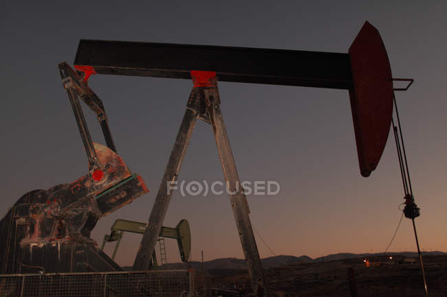 Vista de ángulo bajo de la bomba en el campo de petróleo al atardecer - foto de stock