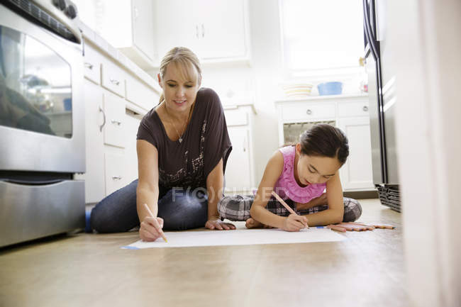 Madre e hija sentadas en el suelo de la cocina y dibujo - foto de stock