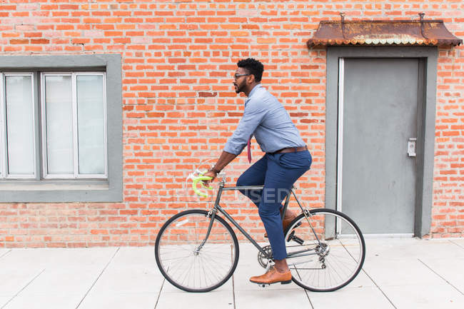 Vista laterale del giovane uomo in bicicletta lungo il marciapiede — Foto stock