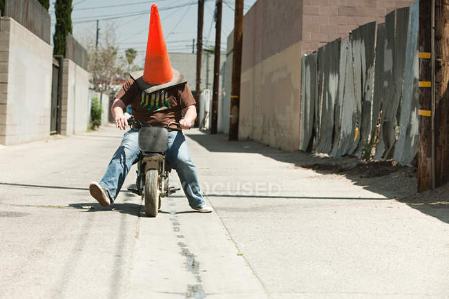 Hombre con cono de tráfico en la cabeza, montar en moto — Stock Photo