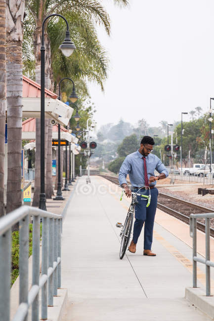 Jovem empresário ciclista olhando para assistir na plataforma da estação ferroviária — Fotografia de Stock