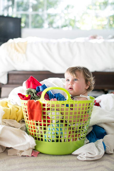 Female toddler sitting in basket amongst laundry — Stock Photo