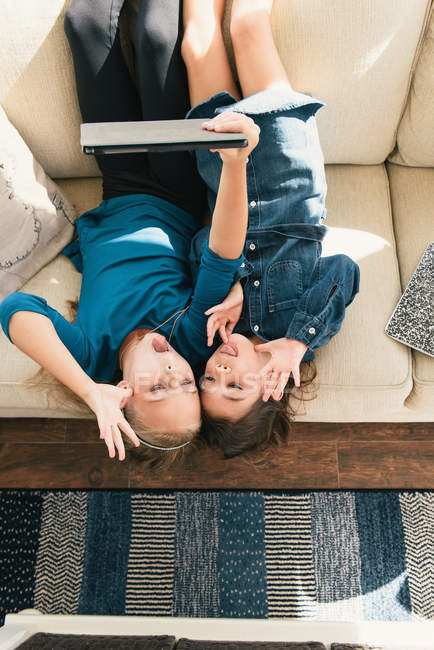 Девочки вверх ногами на диване с помощью цифрового планшета, чтобы сделать селфи — стоковое фото