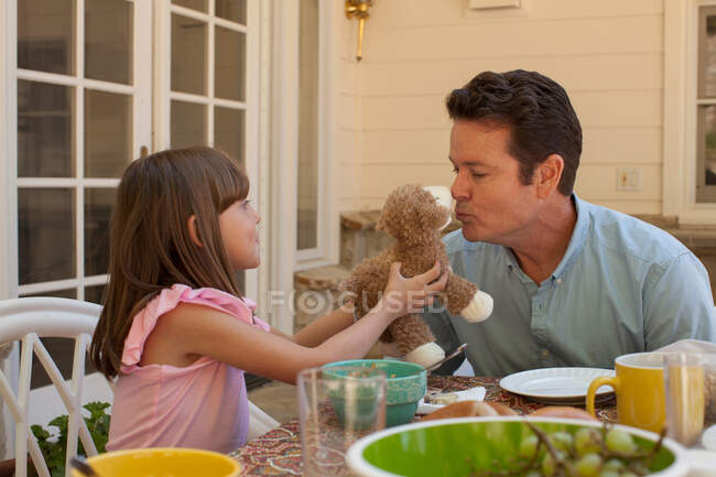 Young girl holding teddy bear for father to kiss — Stock Photo