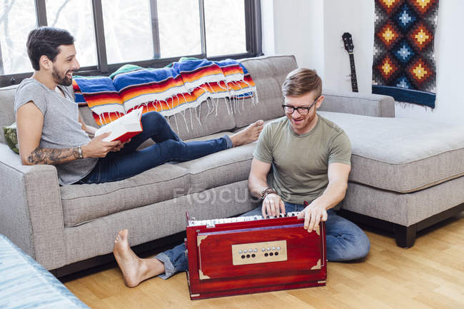 Male couple at home, Young man on sofa watching his partner play musical instrument — Stock Photo