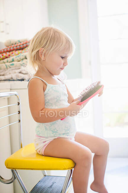 Chica sentada en silla amarilla sosteniendo cepillo - foto de stock