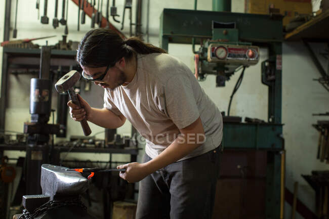 Male metalsmith hammering red hot metal on workshop anvil — Stock Photo