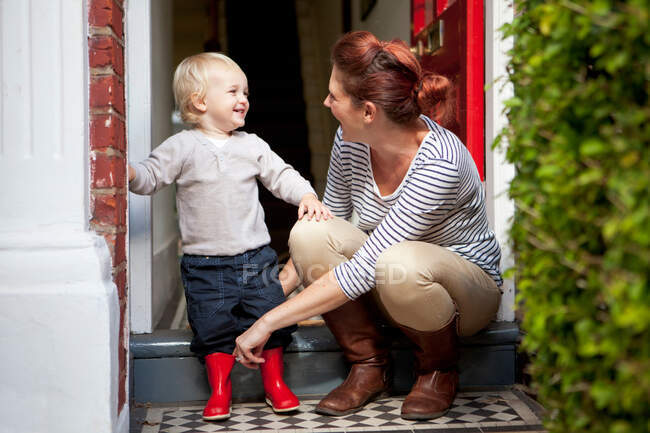 Kleiner Junge lächelt, nachdem Mutter ihm geholfen hat, Gummistiefel anzuziehen — Stockfoto