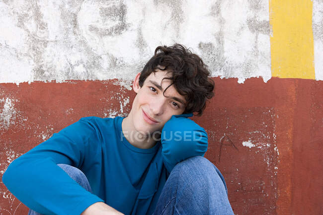 Adolescente sentado contra una pared - foto de stock