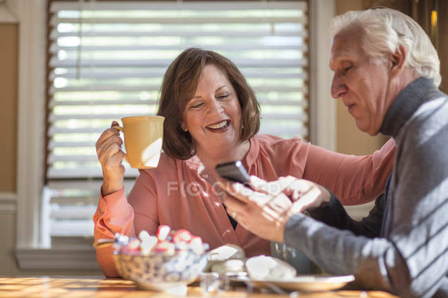 Старша пара дивиться на оновлення смартфона за кухонним столом — стокове фото